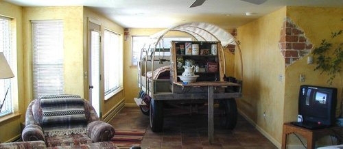A unique living room featuring a covered wagon as a centerpiece, with a sofa and TV in a cozy, yellow-walled space.