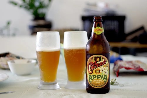 Two glasses of beer beside a bottle of Colorado Appia on a table with snacks in the background.