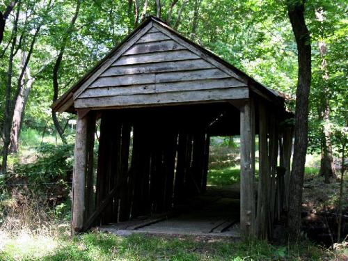 A rustic wooden covered bridge surrounded by trees, with a dark entrance leading into the structure.