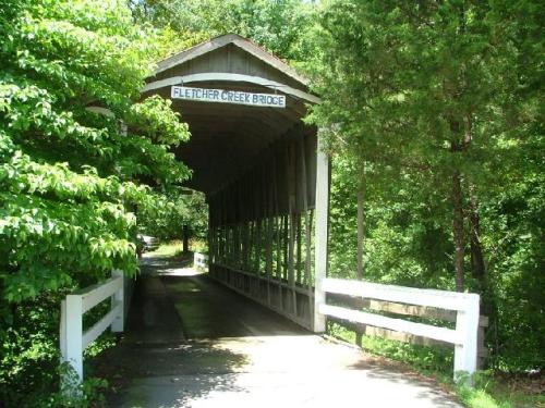 A covered bridge named Fletcher Creek Bridge surrounded by lush greenery and trees.