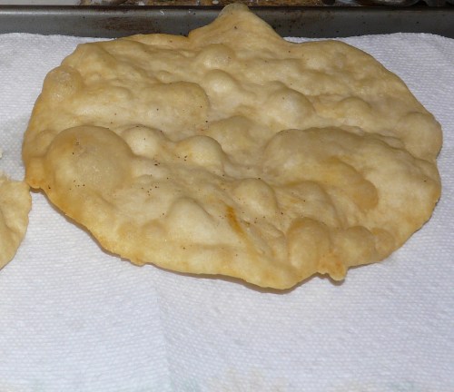 A golden-brown, puffy fried bread resting on a paper towel, showcasing a light, airy texture.