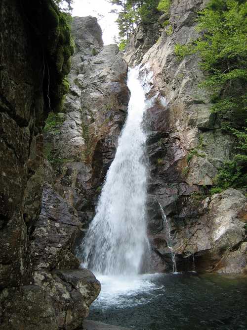 A cascading waterfall flows down rocky cliffs, surrounded by lush greenery and natural stone formations.