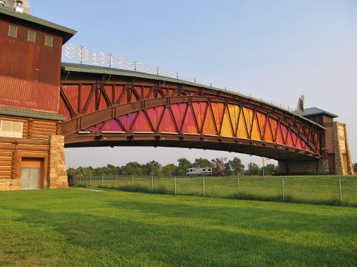 A colorful arched bridge spans over a grassy area, adjacent to a rustic building with wooden and stone elements.