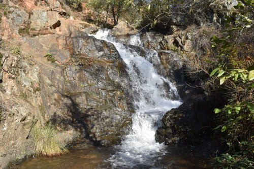 A small waterfall cascading over rocky terrain, surrounded by greenery and natural scenery.