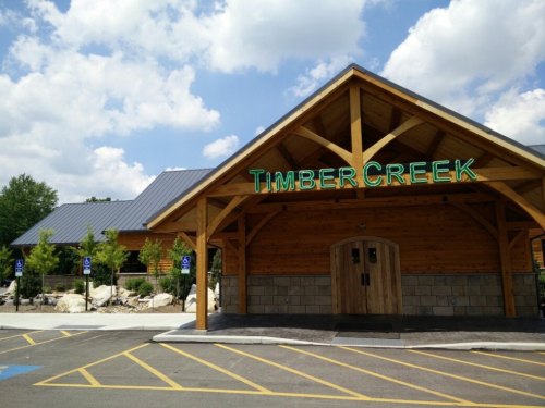 Exterior of Timber Creek restaurant featuring a wooden structure and green signage under a blue sky with clouds.