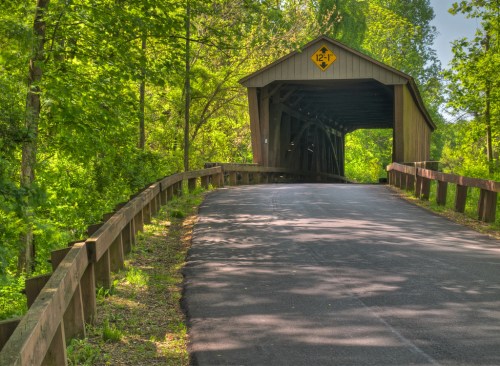 A scenic view of a covered bridge surrounded by lush greenery and a winding road leading to it.