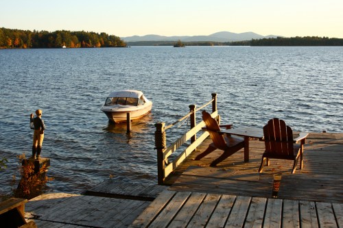 A serene lakeside scene at sunset, featuring a boat, a dock, and a wooden chair overlooking the water.