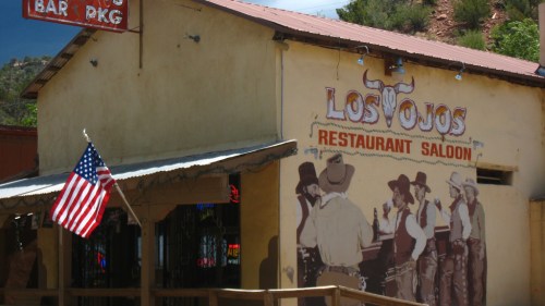 A rustic restaurant saloon with a mural of cowboys and an American flag outside.