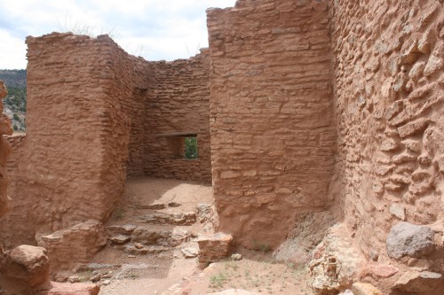 Ruins of an ancient stone structure with weathered walls and a small window, surrounded by rocky terrain.
