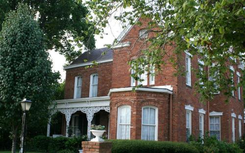 A charming brick house with white trim, surrounded by greenery and featuring a decorative porch.