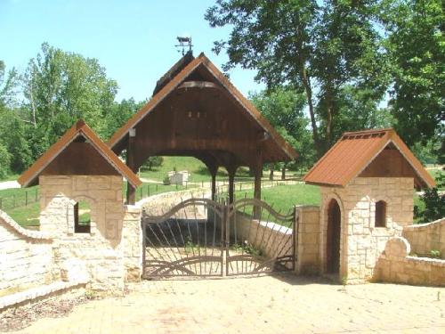 A rustic stone entrance with a wooden roof and decorative gates, surrounded by lush greenery and trees.