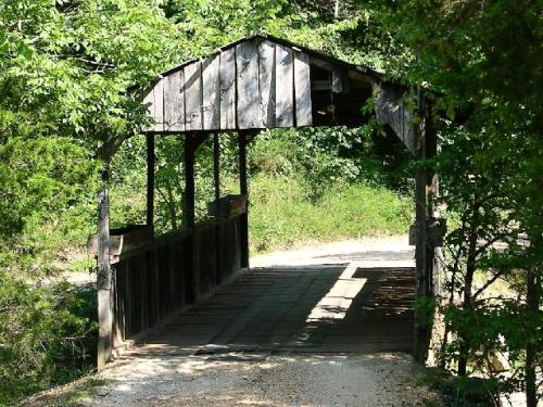 A rustic wooden covered bridge surrounded by lush greenery and a gravel path.