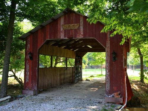 A rustic red covered bridge surrounded by lush green trees and gravel path.