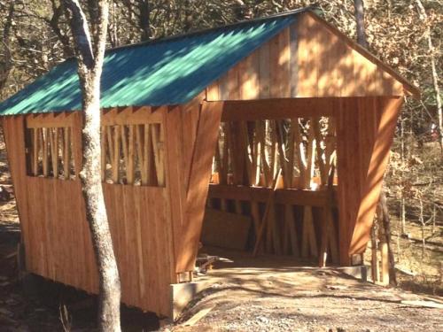 A wooden structure with a green roof, partially open, surrounded by trees in a natural setting.