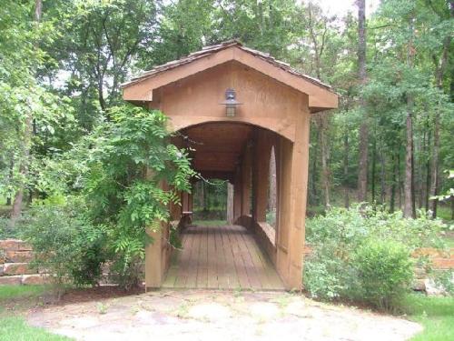 A wooden covered bridge surrounded by lush greenery and trees, leading into a serene natural setting.