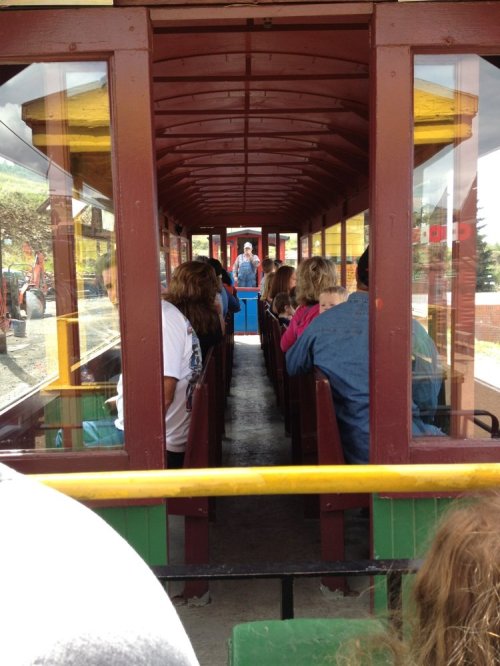 Interior view of a train car with passengers seated on either side, facing a conductor at the front.