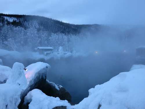 A serene winter scene of a steaming hot spring surrounded by snow-covered rocks and trees in a misty landscape.