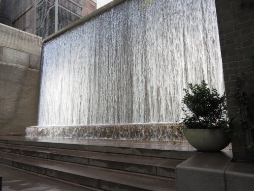A serene water wall cascading down a stone structure, with a small plant in a pot nearby.