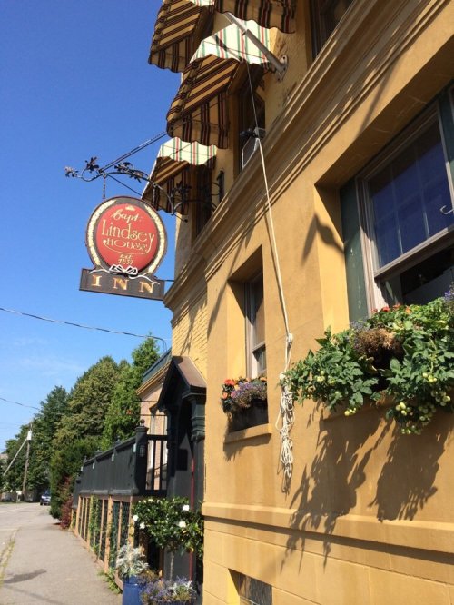 A yellow inn with flower boxes, striped awnings, and a hanging sign that reads "Lindsey Inn."