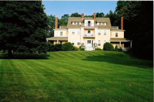 A large yellow house with multiple balconies, surrounded by a lush green lawn and trees.