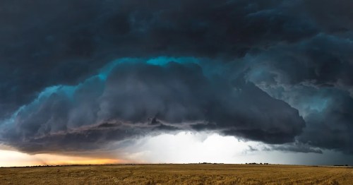 Dramatic storm clouds loom over a vast, open field, with a hint of light peeking through the dark sky.