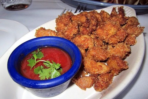 A plate of crispy fried shrimp served with a small bowl of red dipping sauce garnished with cilantro.