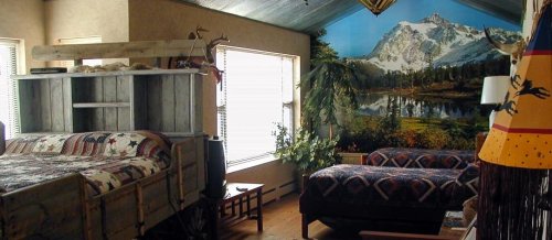 Cozy bedroom featuring a wooden bed, patterned bedding, a mural of mountains, and a comfortable seating area.