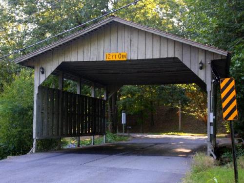 A wooden covered bridge with a height clearance sign reading "12 FT 0 IN" over a road surrounded by trees.