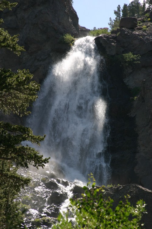 A cascading waterfall flows down rocky cliffs, surrounded by lush greenery and trees.