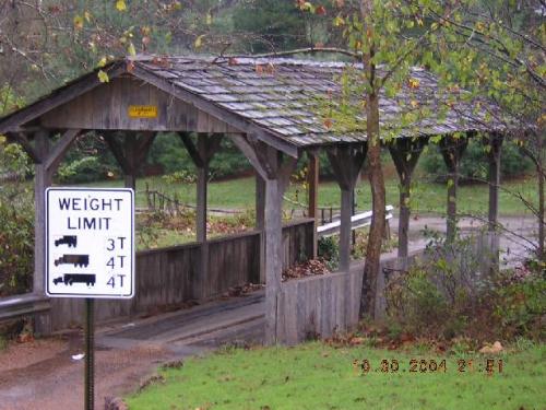 A wooden covered bridge with a weight limit sign for vehicles, surrounded by trees and greenery.