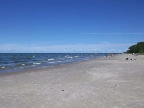 A sandy beach with gentle waves, under a clear blue sky, and a few people enjoying the shoreline in the distance.