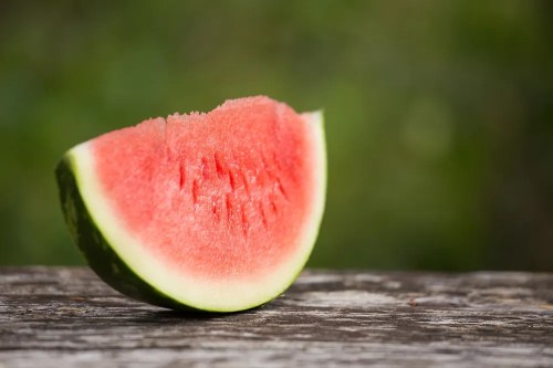 A slice of watermelon rests on a wooden surface, showcasing its juicy red flesh and green rind.