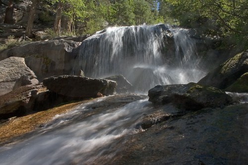 A serene waterfall cascading over rocks, surrounded by lush greenery and sunlight filtering through the trees.