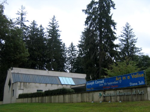 Exterior of the National Museum of Art, featuring a sign for the Joseph Cornell exhibit and surrounded by tall trees.