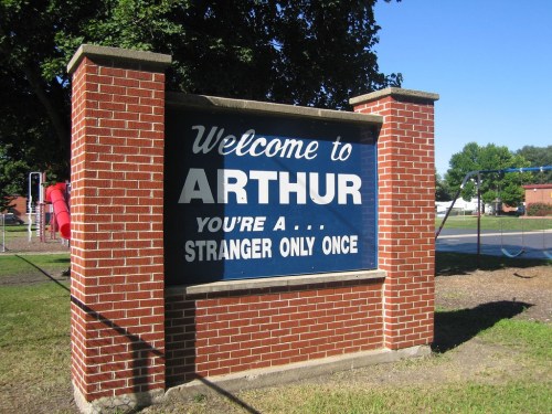 Welcome sign for Arthur, reading "You're a stranger only once," with a playground visible in the background.