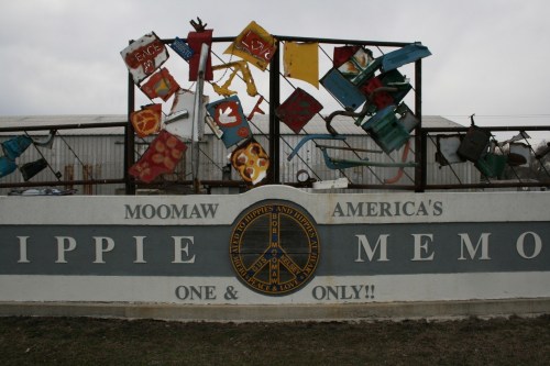 Colorful metal art installation with peace symbols and a sign reading "Moomaw America's Hippie Memorial."