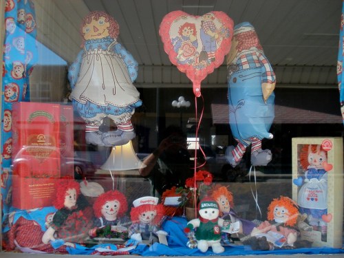 A display of various rag dolls and balloons in a shop window, featuring colorful characters and decorations.