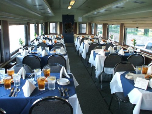 Interior of a dining car with neatly set tables, white tablecloths, and drinks, creating an elegant dining atmosphere.