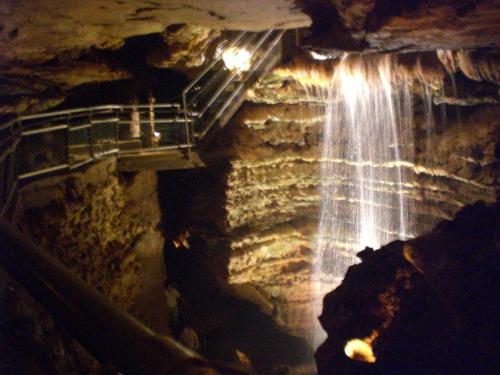 A dimly lit cave with a waterfall cascading down rocks, and a metal walkway in the background.
