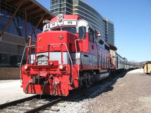 A red and silver train engine parked on tracks beside a modern building.