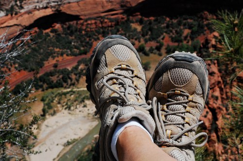A pair of hiking shoes resting on a ledge, overlooking a scenic canyon with greenery and a river below.