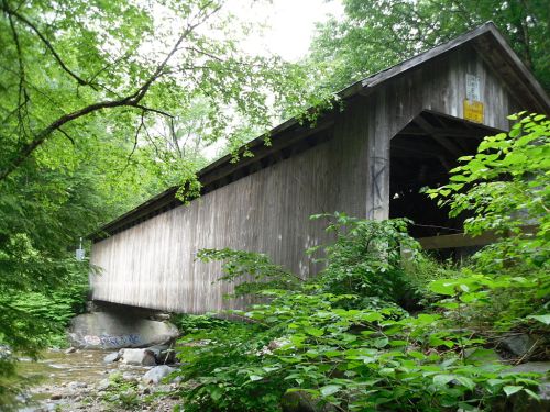 A wooden covered bridge surrounded by lush greenery and trees, spanning a small creek.