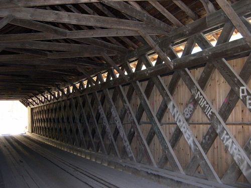 Interior view of a covered bridge, featuring wooden beams and a light source at the far end.