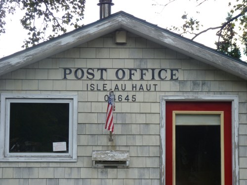 A small, weathered building with a sign reading "Post Office" and an American flag, located on Isle au Haut.