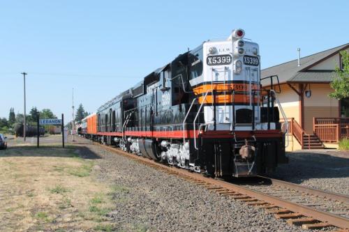 A vintage train with orange and black stripes parked on tracks near a station in Lebanon, surrounded by grass and trees.