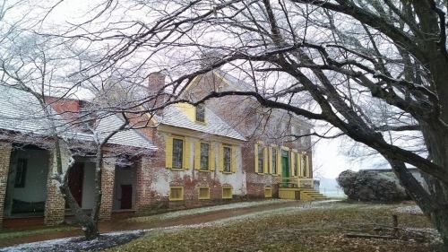 A historic house with yellow trim, surrounded by bare trees and light snow, creating a serene winter scene.