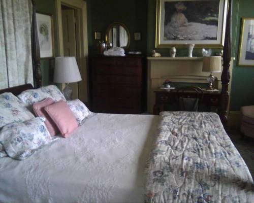 A cozy bedroom with a large bed, floral bedding, green walls, and a dresser, featuring artwork and soft lighting.
