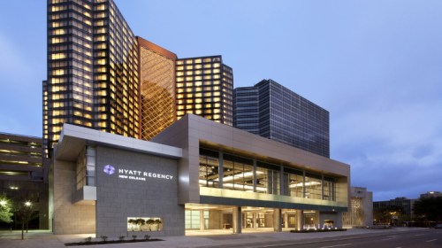 Exterior view of the Hyatt Regency hotel in New Orleans, showcasing modern architecture and illuminated windows at dusk.