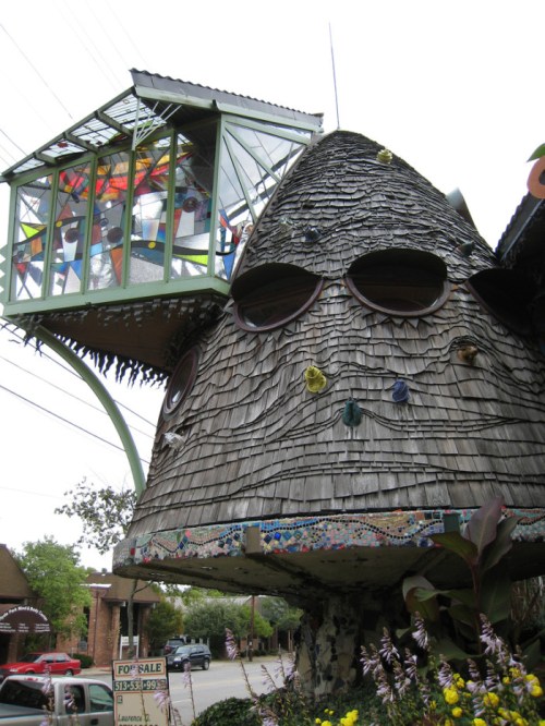 A whimsical, mushroom-shaped house with a glass room on top, surrounded by colorful decorations and greenery.
