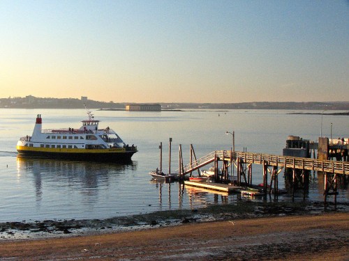 A yellow and white ferry approaches a wooden dock on calm waters during sunrise.